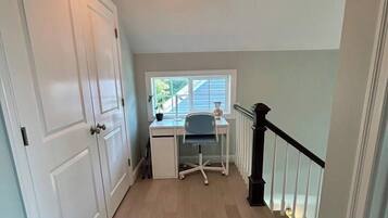 Un couloir étroit avec un bureau et une chaise, une fenêtre donnant sur un paysage agréable et un escalier avec une rampe noire.