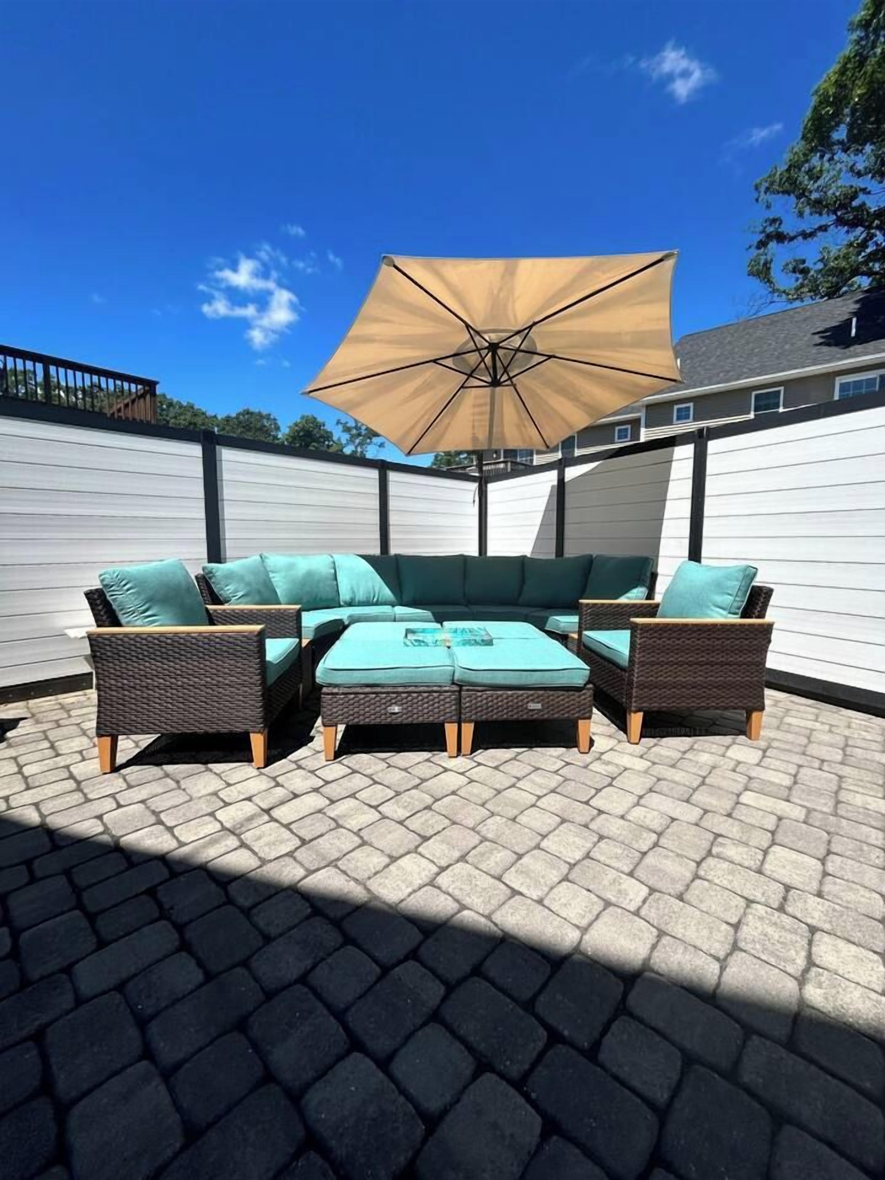 Een terras met een bank, twee fauteuils en een tafel, alles onder een grote parasol.