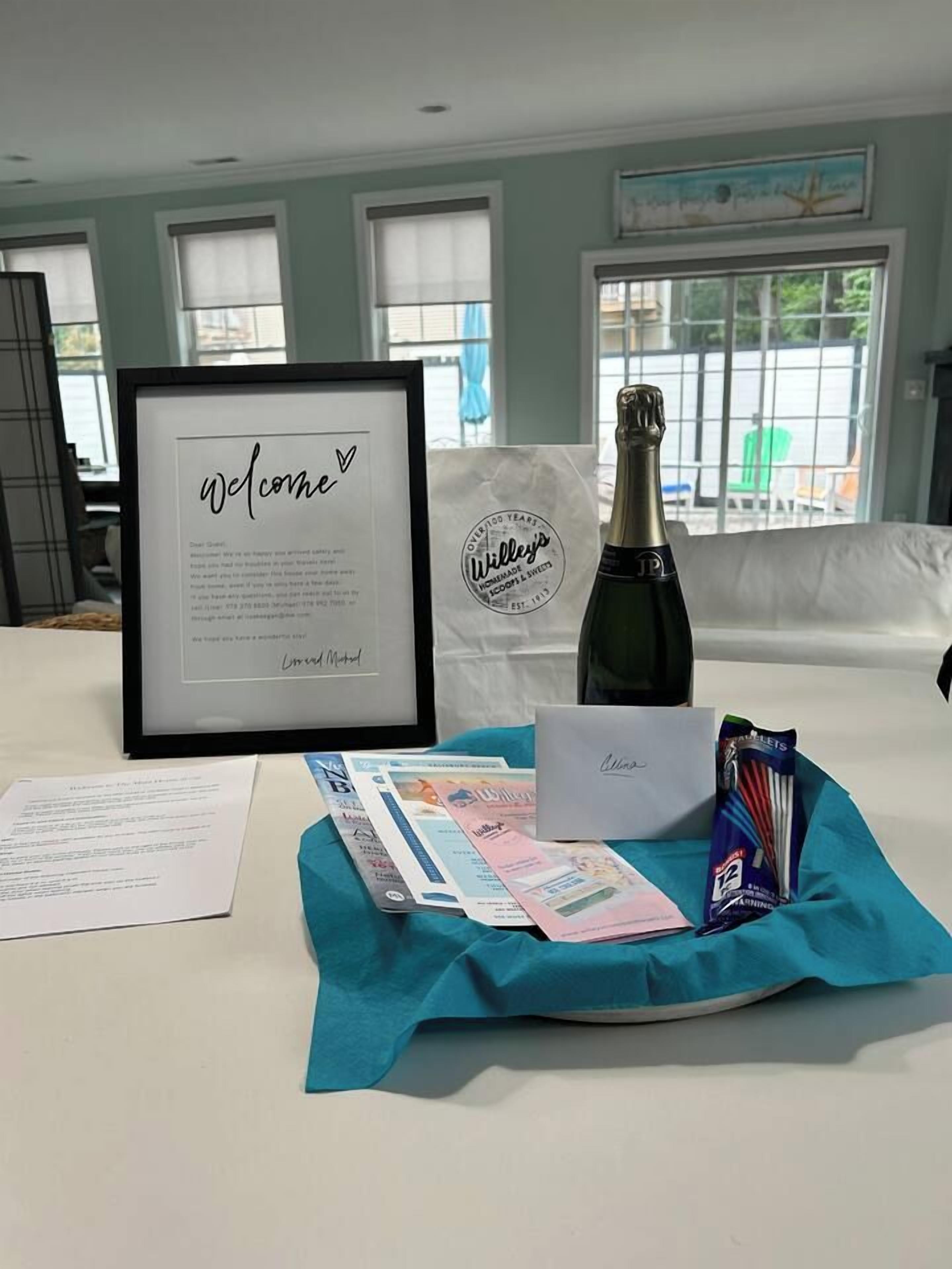 A bed with a framed welcome message, a bottle of champagne, a card, and some brochures.