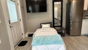 Quarto com cama, televisão de tela plana na parede, geladeira e porta com janela.