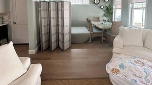 Uma sala de estar com sofá, área de refeições com mesa e cadeiras, e uma parede divisória.