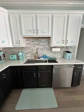 Una cocina con armarios blancos, lavavajillas de acero inoxidable y salpicadero de azulejos.