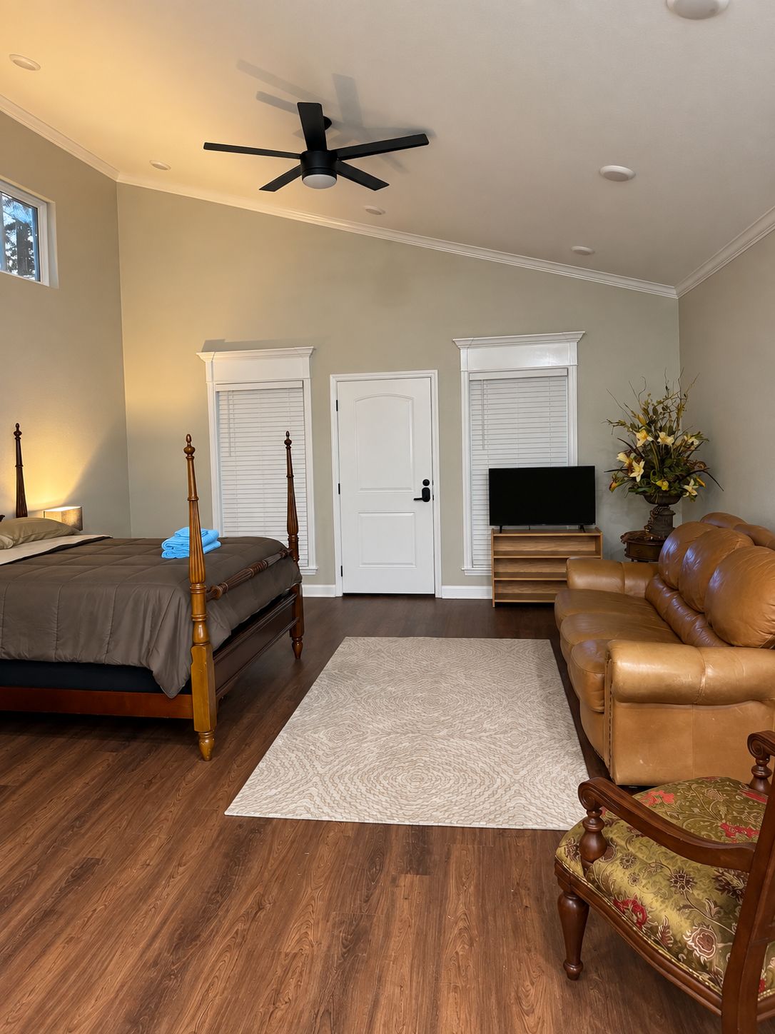 A bedroom with a bed, a ceiling fan, a TV, a sofa, and a door.