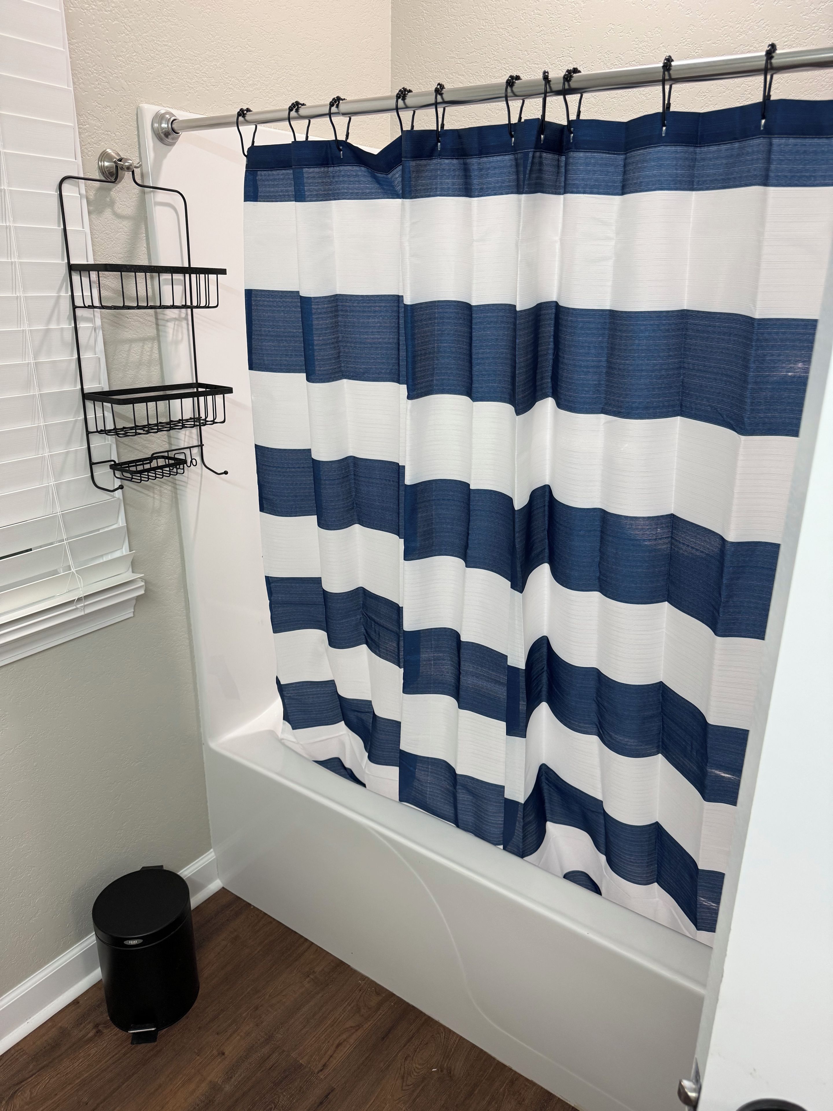 A bathroom with a striped shower curtain, a black wastebasket, and a metal shelf unit.