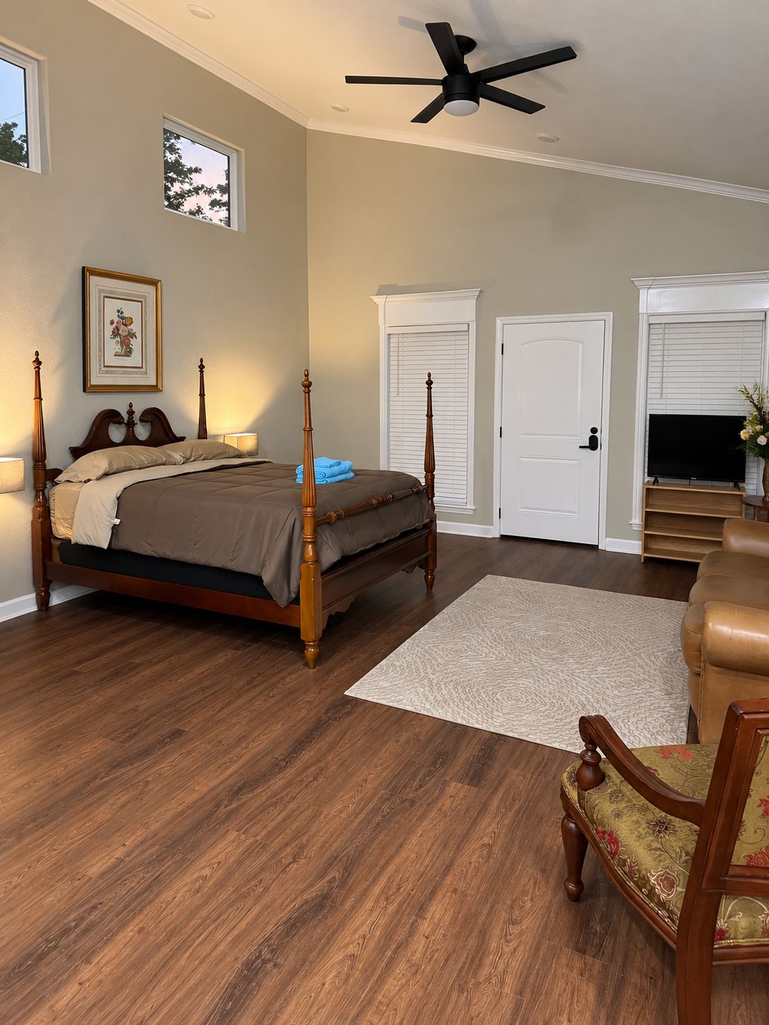 A bedroom with a four-poster bed, a ceiling fan, a television, and a fireplace.
