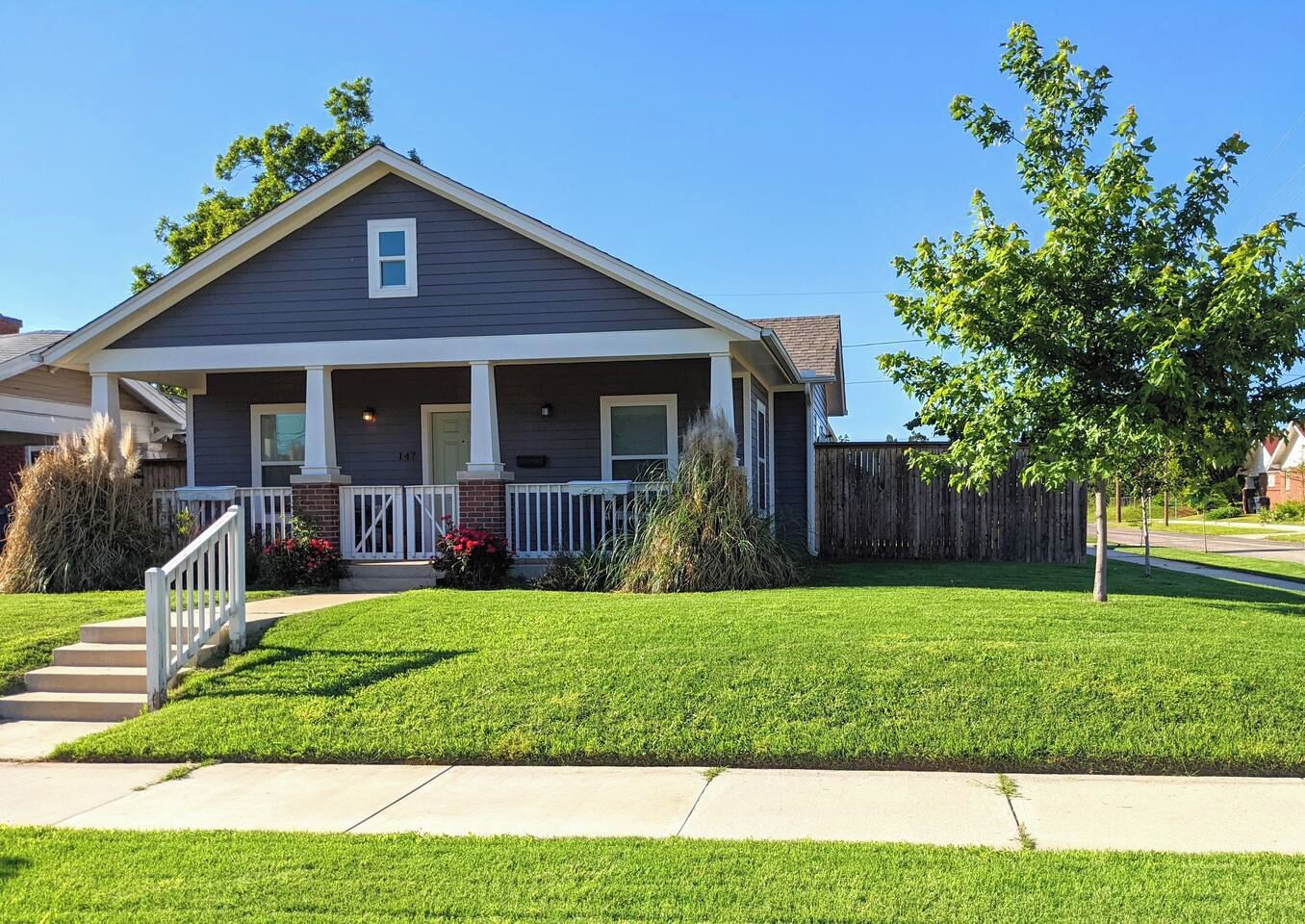A single-story house with a front porch, a small front yard, and a wooden fence.