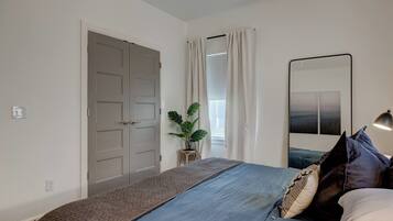 Une chambre à coucher avec un lit, une lampe de chevet, un miroir, une fenêtre avec des rideaux et une porte.