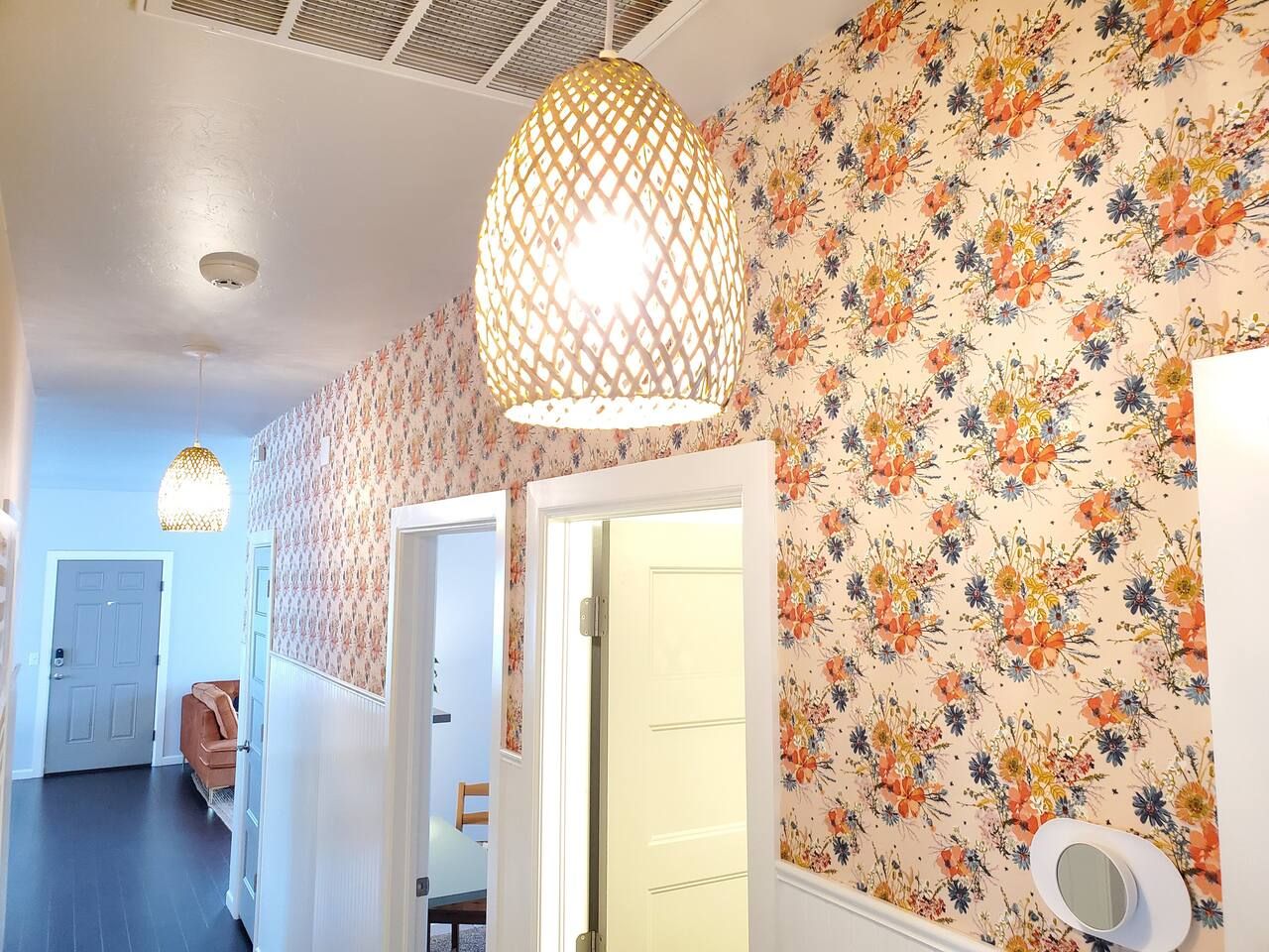 Un couloir orné d’un papier peint à motifs floraux, un luminaire suspendu et une porte donnant sur une autre pièce.