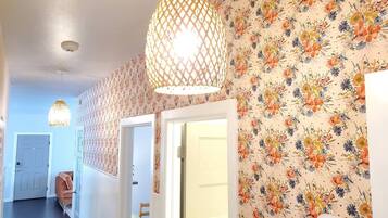 Un couloir orné d’un papier peint à motifs floraux, un luminaire suspendu et une porte donnant sur une autre pièce.