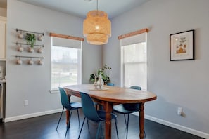Een eetgedeelte met een houten tafel, blauwe stoelen, een hanglamp en een plant aan de muur.