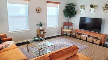 A living room with a sofa, coffee table, TV stand, and a large plant.