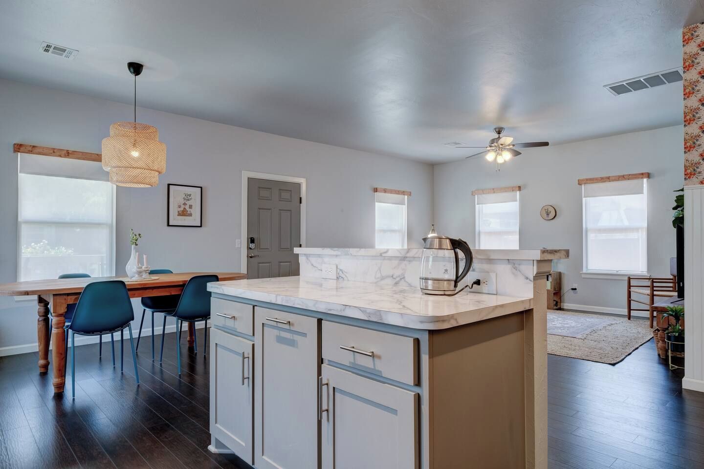 A modern kitchen with a marble countertop, wooden cabinets, and a dining area with blue chairs.