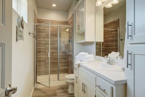 Een moderne badkamer met een douche met glazen wand, een witte wastafel en een grote spiegel.