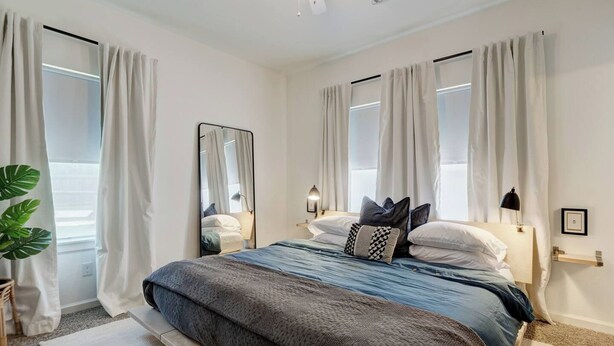 A bedroom with a bed, a nightstand, a mirror, a lamp, and a potted plant. - Best Value, Sleeps 6, Near Downtown & Bricktown (Oklahoma City)