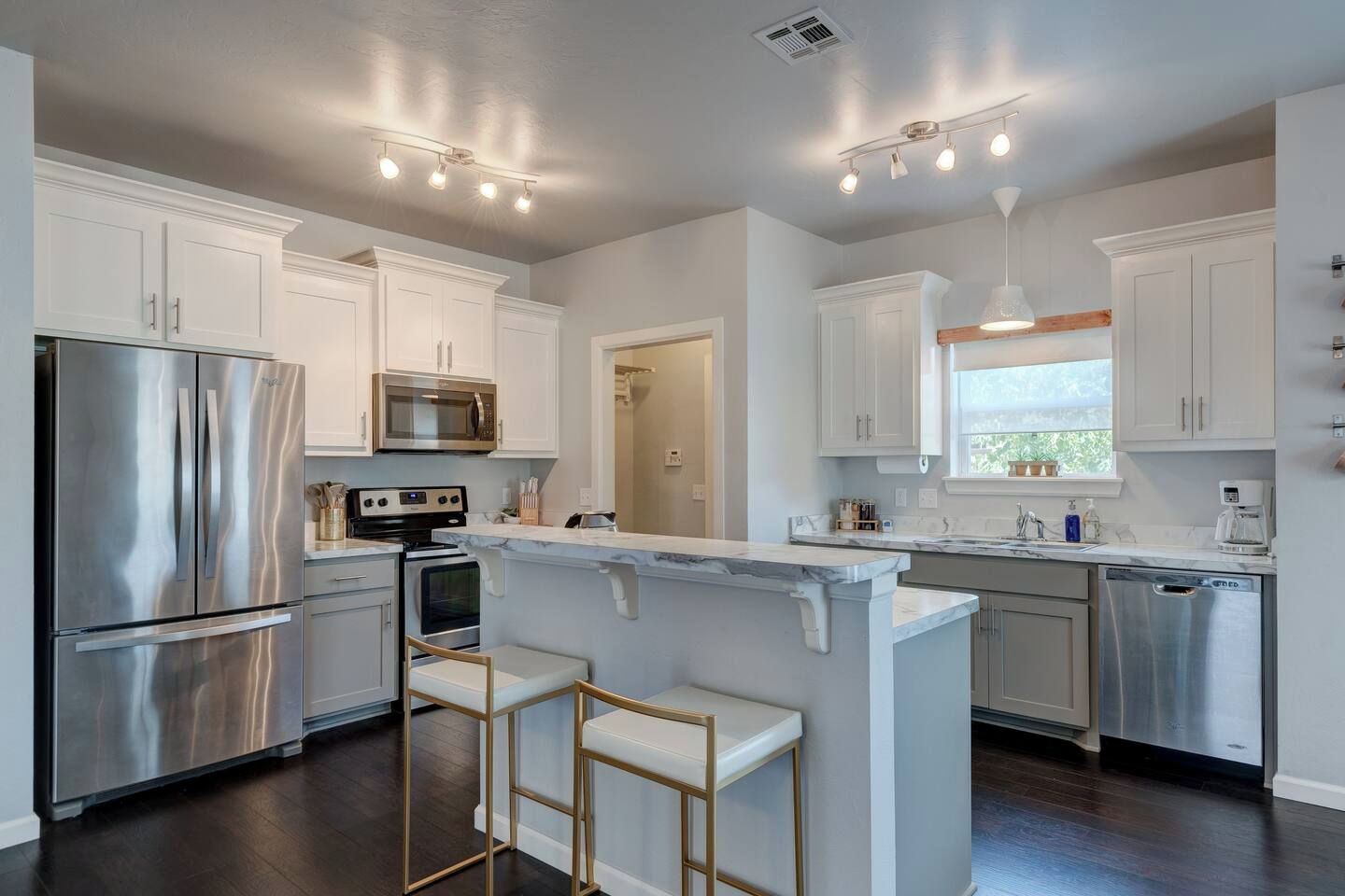 A modern kitchen with stainless steel appliances, white cabinetry, and a marble countertop island.