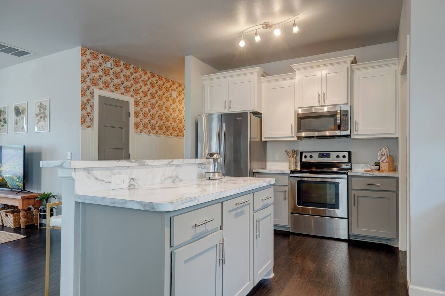 A modern kitchen with white cabinetry, a marble countertop, stainless steel appliances, and a patterned wall.