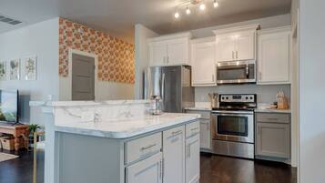 A modern kitchen with white cabinetry, a marble countertop, stainless steel appliances, and a patterned wall.
