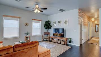 A living room with a sofa, TV, ceiling fan, and a large window.