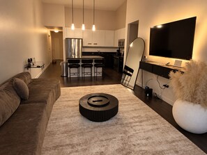 Een moderne woonkamer met een bank, een salontafel, een televisie en een keuken op de achtergrond.