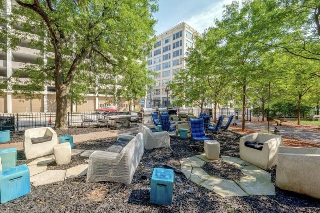 Un espace extérieur aménagé avec différents types de chaises et de tables, entouré d’arbres et avec un bâtiment en arrière-plan.