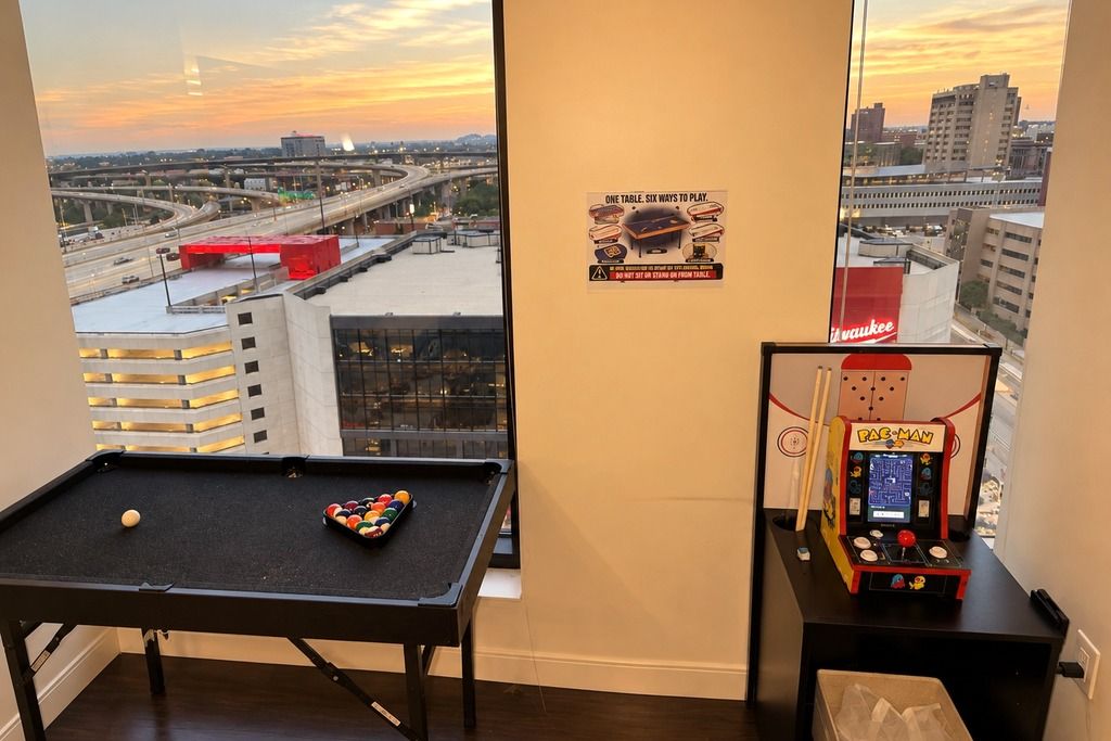 A pool table with a city view, a Pac-Man arcade machine, and a sign about table etiquette.