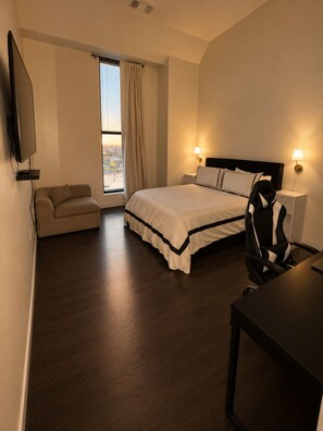 A hotel room with a bed, a sofa, a desk, a chair, and a TV.