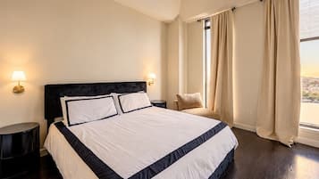 Une chambre d’hôtel avec un grand lit, deux tables de chevet, une chaise et une fenêtre avec des rideaux.