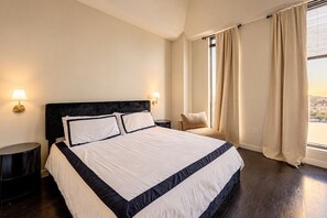 Een hotelkamer met een groot bed, twee nachtkastjes, een stoel en een raam met gordijnen.