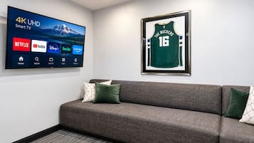 Un téléviseur intelligent 4K UHD avec accès aux services de diffusion en continu, un maillot de sport encadré et un canapé gris avec des coussins.