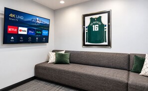 Een 4K UHD smart-tv met streamingdiensten, een ingelijst sportshirt en een grijze bank met kussens.