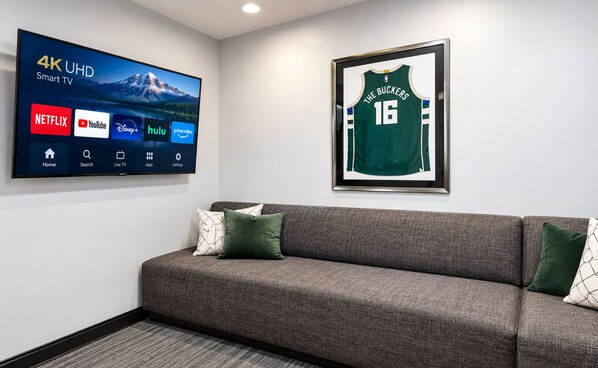 A 4K UHD smart TV with streaming services, a framed sports jersey, and a gray sofa with cushions.