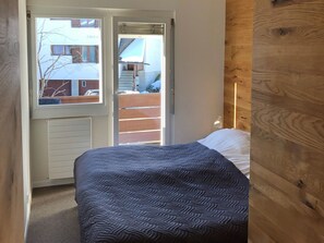 Ein Schlafzimmer mit einem Bett, einem Holz-Kopfteil, einem Fenster und Blick auf ein Gebäude.