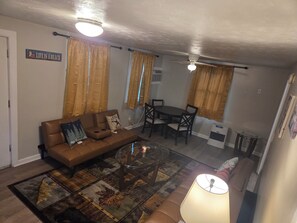 A living room with a brown sofa, a glass coffee table, a dining table with chairs, and a ceiling fan. - Amazing 1-bedroom Condo with AC in cozy Saco (Saco)