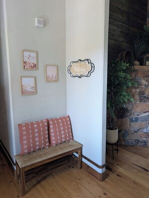 Un banco de madera con cojines, un cartel de bienvenida, marcos con fotografías y una planta en maceta.