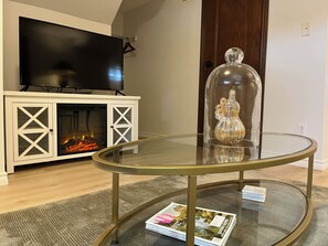 A living room with a flat-screen TV, a glass coffee table, and a fireplace.