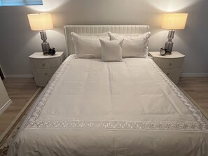 A neatly made bed with a white headboard and two bedside tables with lamps, a clock, and a small decorative item on each. - Lovely 1-bedroom apartment in Sault Ste. Marie (Sault Ste. Marie)