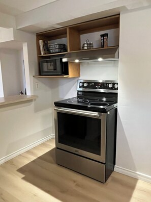 A kitchen with a stainless steel stove, a microwave, and wooden shelves above. - Lovely 1-bedroom apartment in Sault Ste. Marie (Sault Ste. Marie)