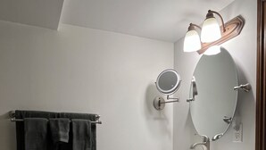 Un baño con un lavamanos blanco, un espejo y un perchero con dos toallas.