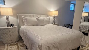 Una cama bien hecha con edredón blanco y almohadas, flanqueada por dos mesitas de noche con lámparas y un reloj despertador.