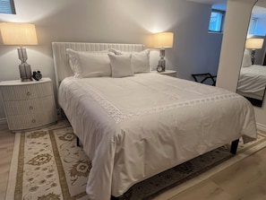 Ein ordentlich bezogenes Bett mit weißer Decke und Kissen, begleitet von zwei Nachttischen mit Lampen und einem Wecker.