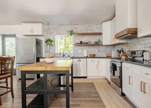 Una cucina moderna con pensili bianchi, un frigorifero in acciaio inossidabile, un tavolo da pranzo in legno e una pianta pensile.