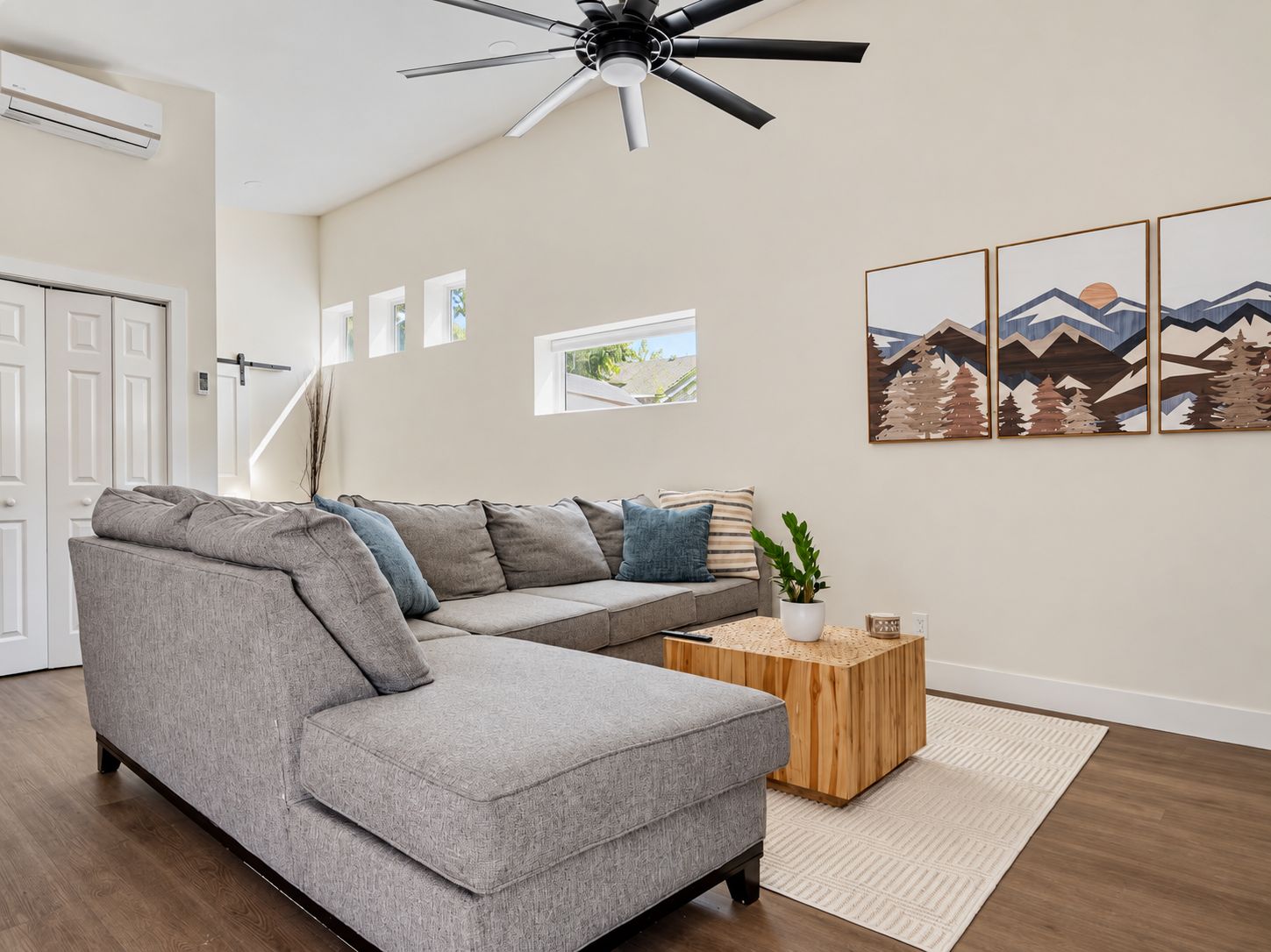Un salon moderne avec un canapé d’angle gris, une table basse en bois et un ventilateur de plafond.