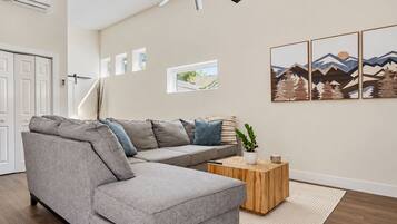 Un salon moderne avec un canapé d’angle gris, une table basse en bois et un ventilateur de plafond.