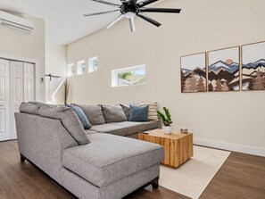 Una sala de estar moderna con un sofá seccional gris, una mesa de centro de madera y un ventilador de techo.