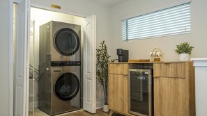 A laundry room with two stacked washers and dryers, a coffee maker, a small refrigerator, and a window with blinds. - 4BR Themed Villa Pool & Cinema Balmoral Resort (Haines City)