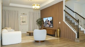 Ein modernes Wohnzimmer mit Sofa, Fernseher, einer Treppe und einer Chandelier.