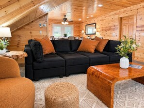 Ein gemütliches Zimmer mit einem schwarzen Ecksofa, einem Holztisch und einem gewebten Pouf.