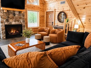 A cozy log cabin interior with a stone fireplace, leather sofas, and a television mounted on the wall. - Heated Pool/Cinema/Hot Tub/Game Room/Massage Chair (Broken Bow)