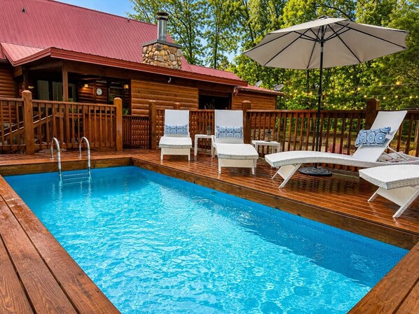 Eine Holzterrasse mit Schwimmbecken, Liegestühlen und Sonnenschirm.