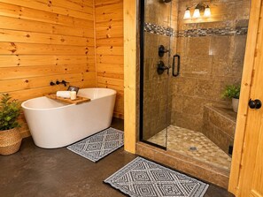 Ein Badezimmer einer Holzhütte mit einer freistehenden Badewanne, einer Duschkabine und gemusterten Teppichen.
